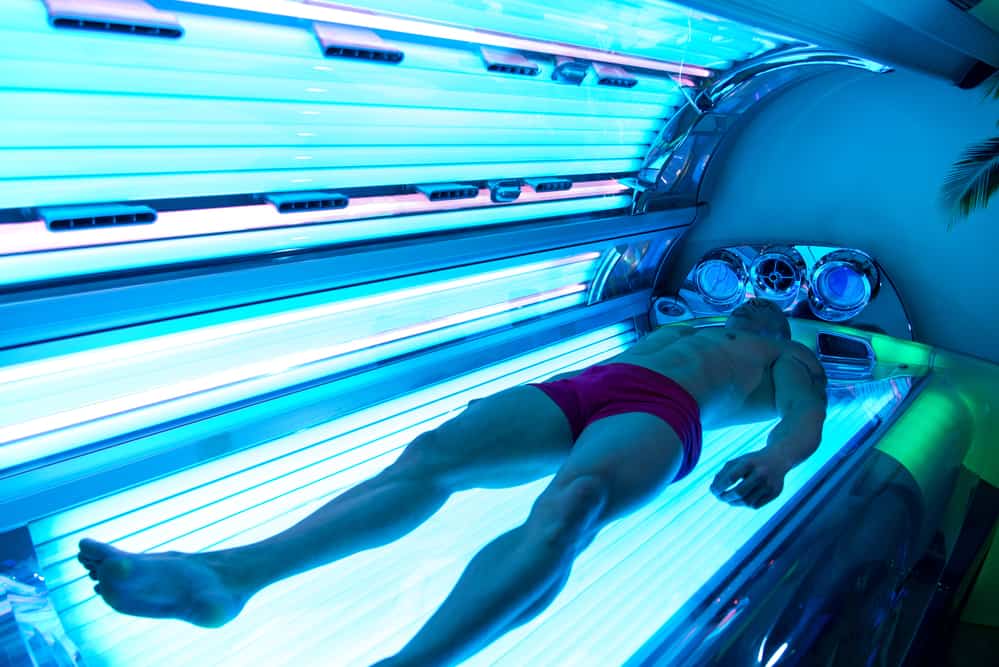 A person lying in a tanning bed with a tattoo visible on their body